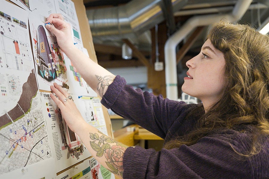 A UO student with her side facing the camera, tacking up a photo on a board