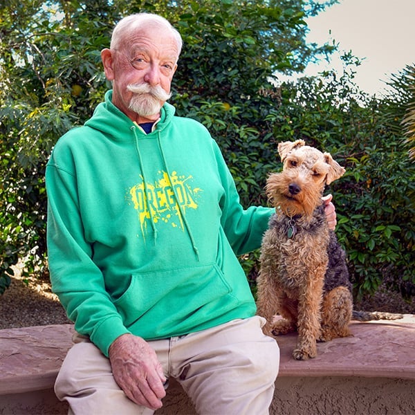 David Sitterson, a UO alum donning a green Oregon sweatshirt, sits next to his Airedale Terrier.
