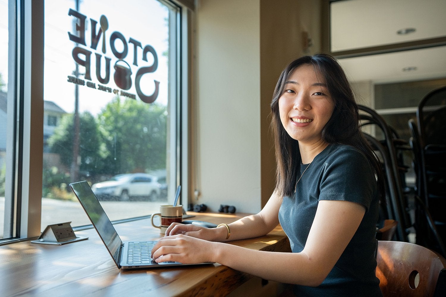Stephanie Yang typing on a laptop with the Stone Soup log on the window in the background