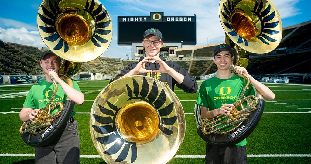 three sousaphone players pose on the UO football field
