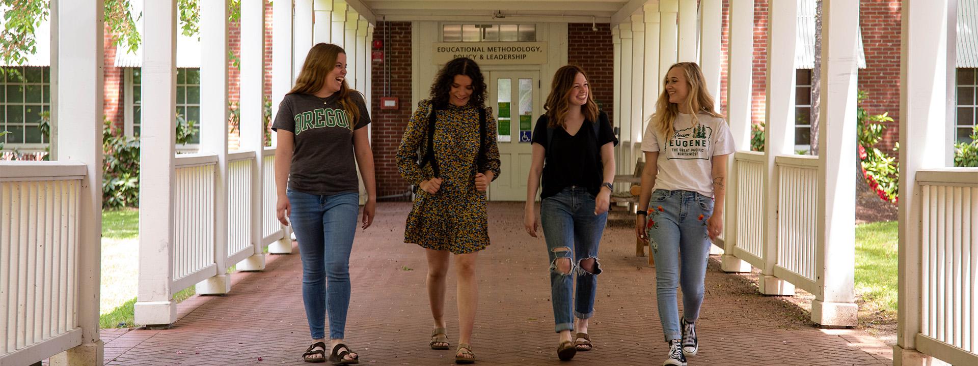 Four UO students laughing as they walk under a covered walkway away from the Educational Methodology, Policy  Leadership building