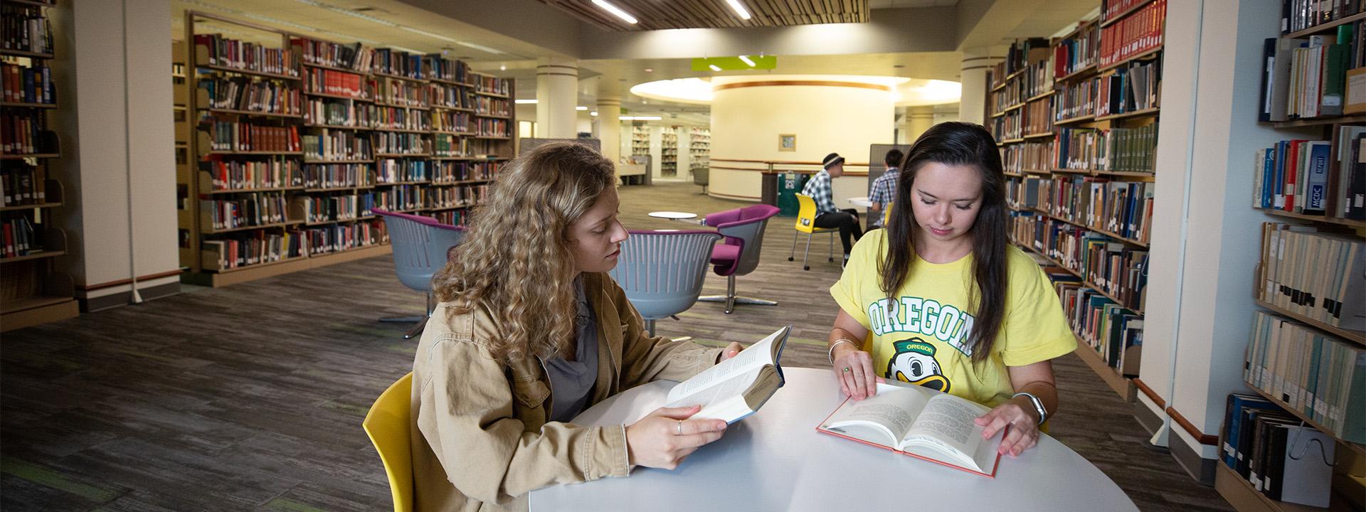 Two UO students read books at a table in a UO library space