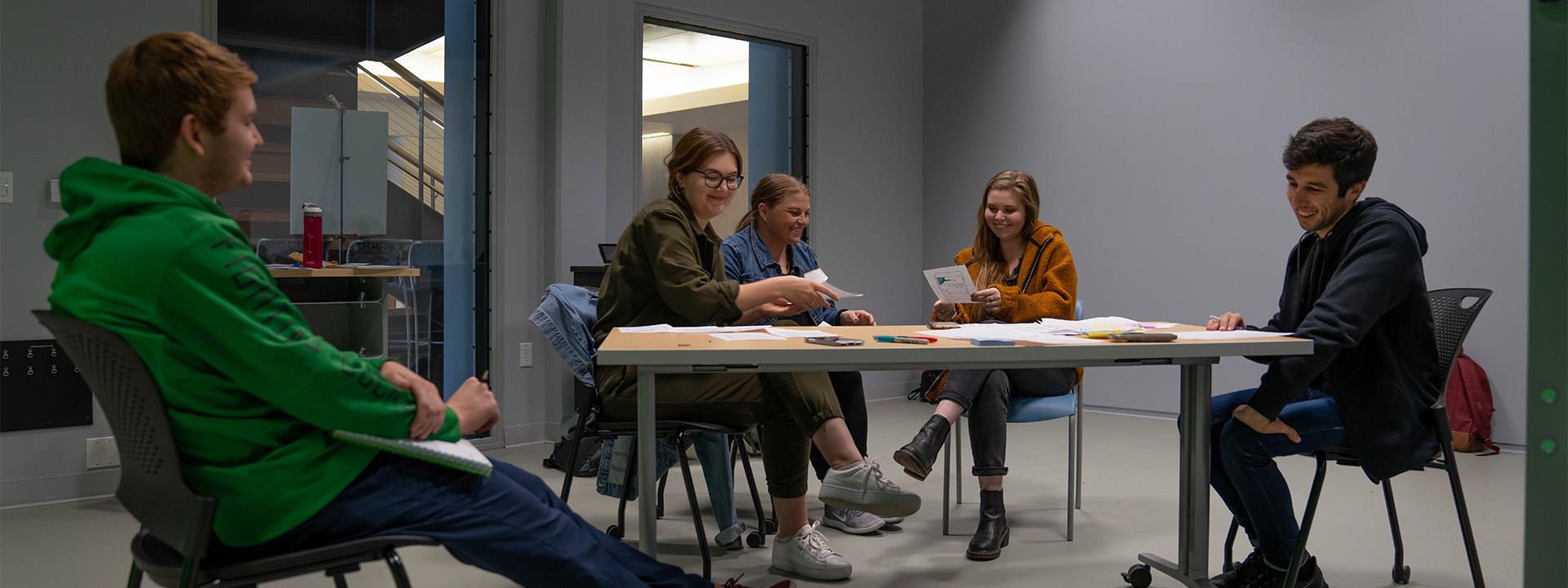 Five UO students sit around a table covered with papers and markers
