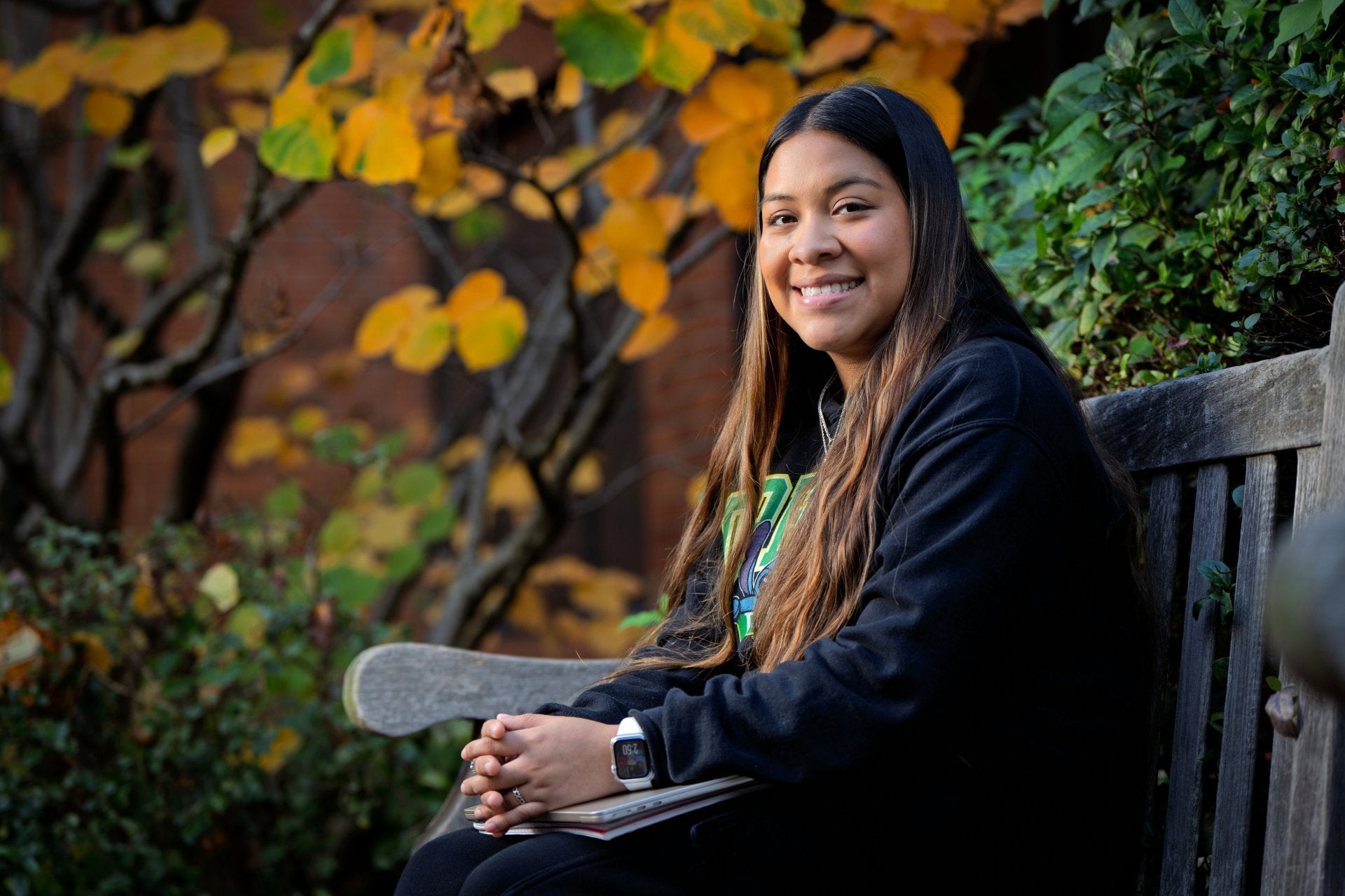 Anahi Cortes sits on a bench at UO with fall leaves in the background