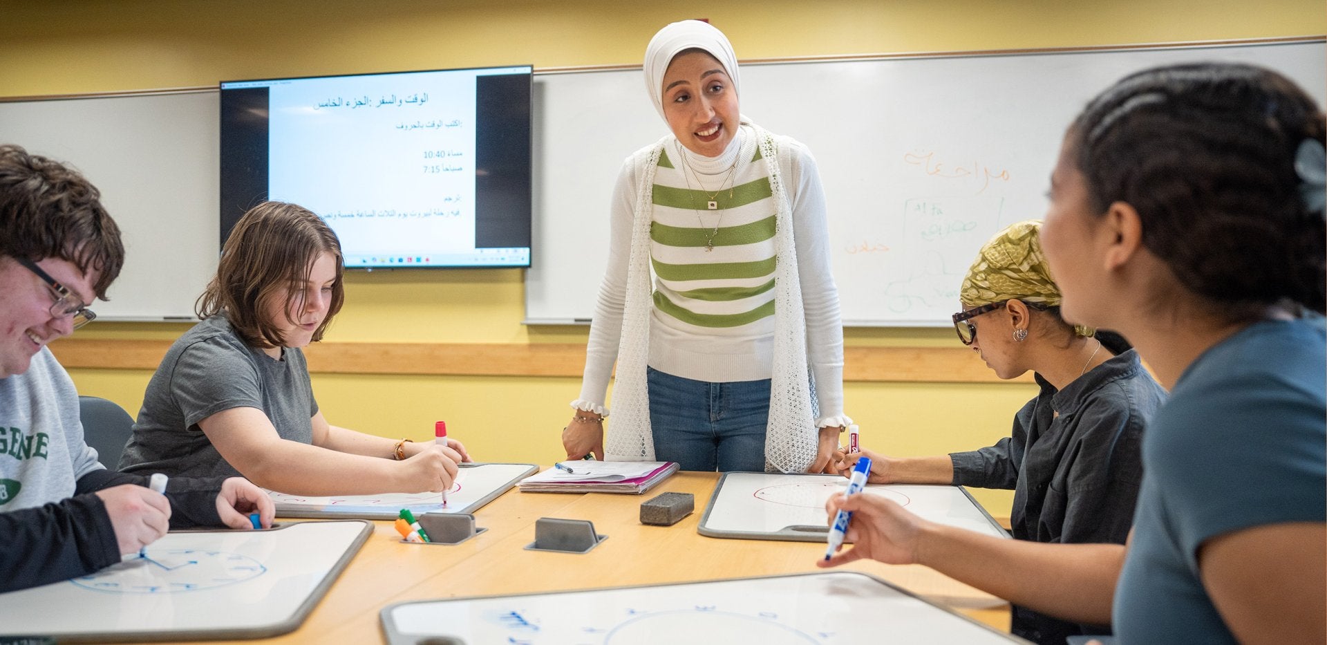Amira Abbid standing in a classroom teaching four college students