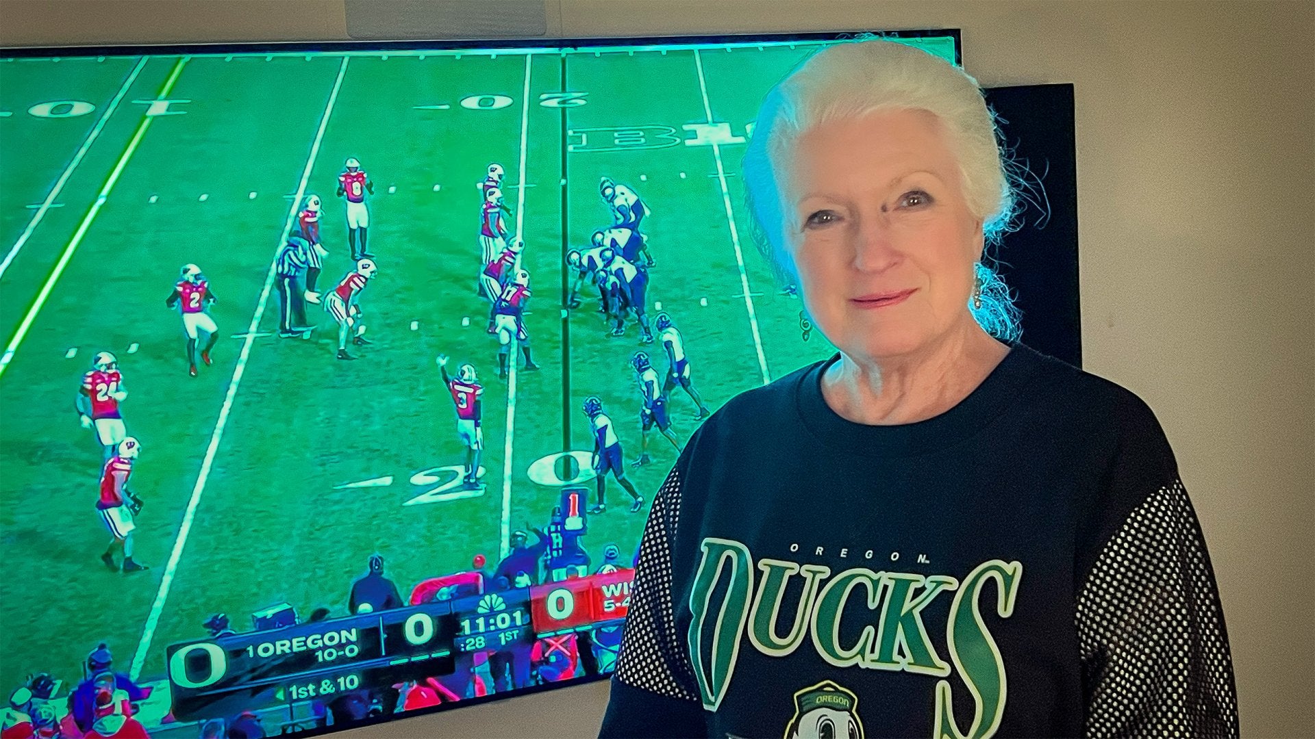 Laurie smiling with the football game behind her with duck gear on
