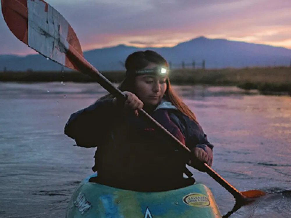 Photo of UO student Ashia Grae Wolf Wilson paddling in a kayak at dusk