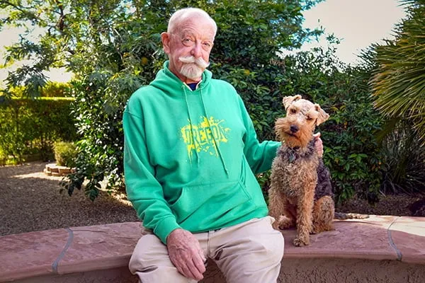 David Sitterson, a UO alum donning a green Oregon sweatshirt, sits next to his Airedale Terrier.