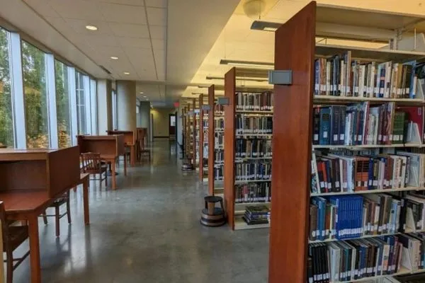 Aisle of UO Portland library with desks next to window on left and library shelves on right