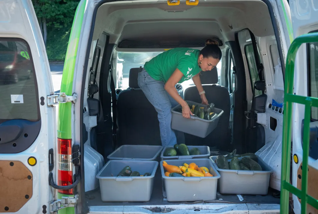 Sarah Van Horn arranges tubs of squash in the back of a cargo van. 