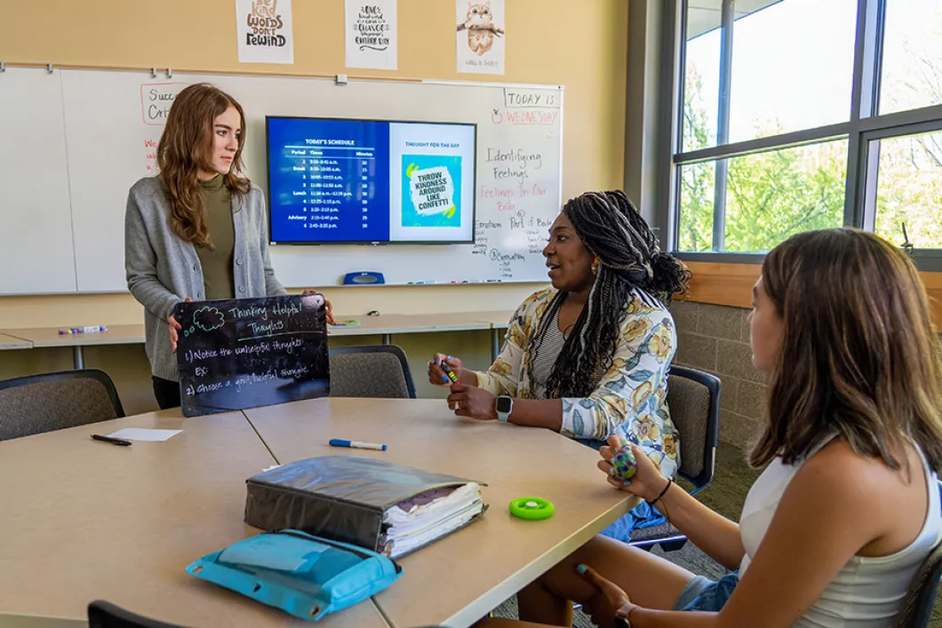 Two adult Ballmer students working with a child in a classroom