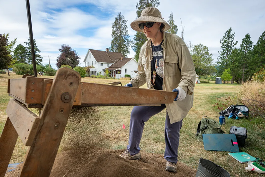 A student in a work hat and jacket working at a wood platform outside