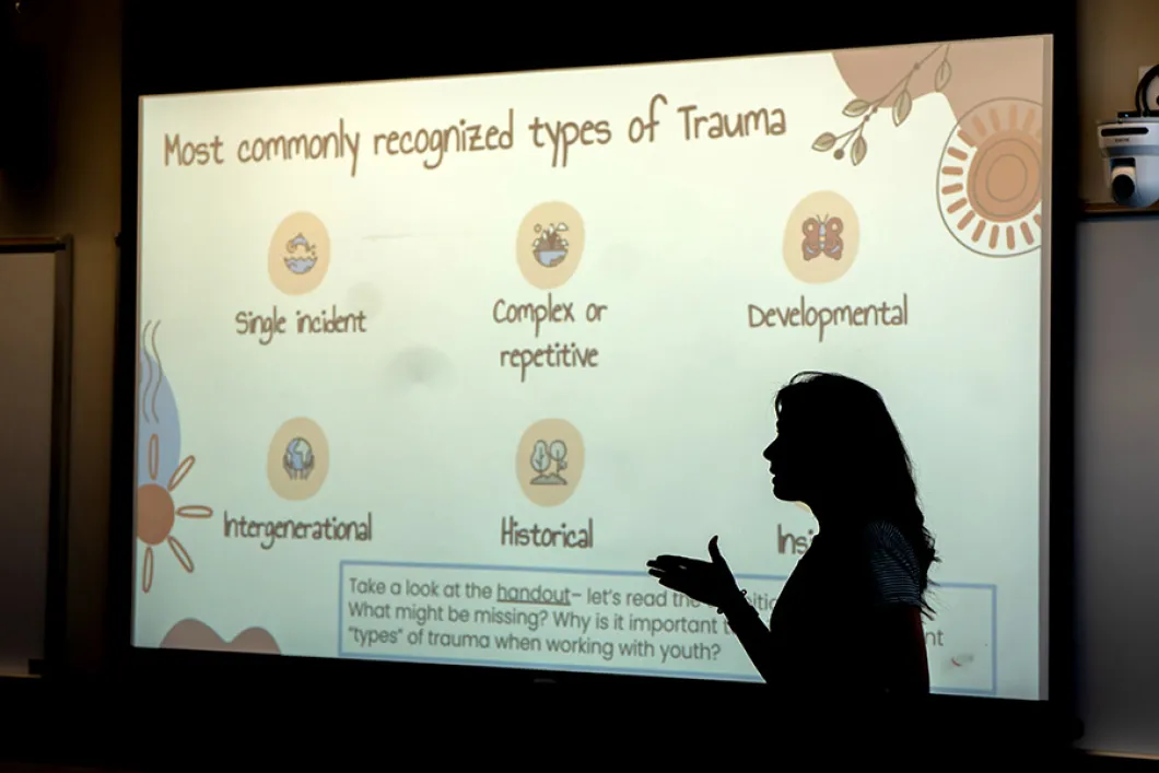 A person standing in front of a presentation projection, with a slide about "Most commonly recognized types of trauma"