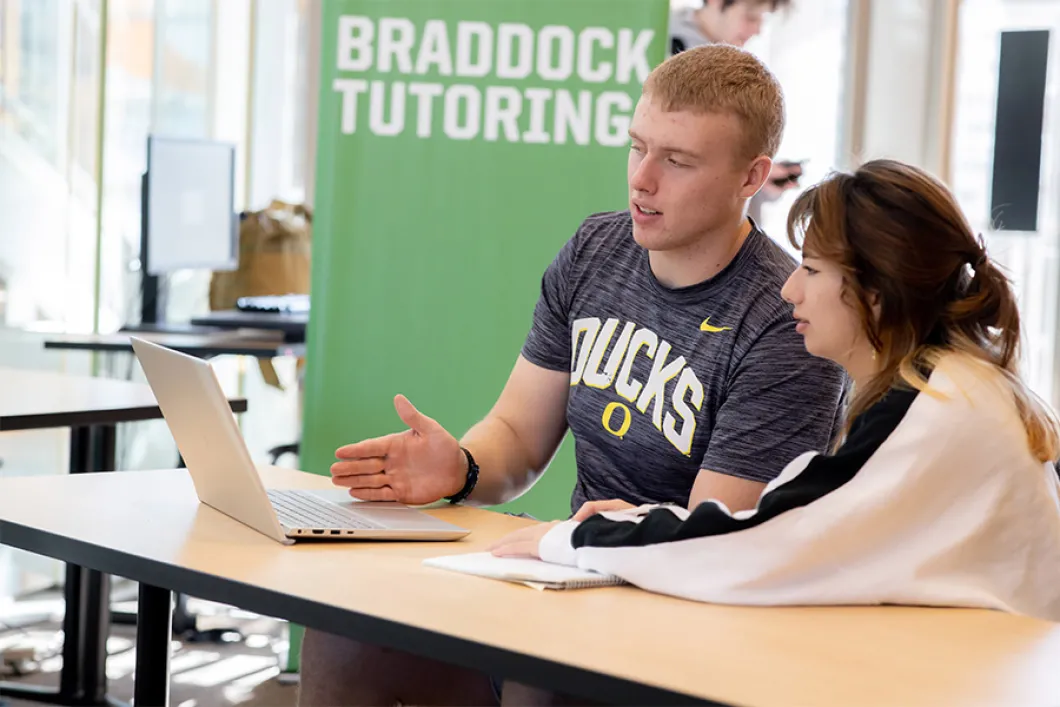 A student and a tutor working on the same laptop