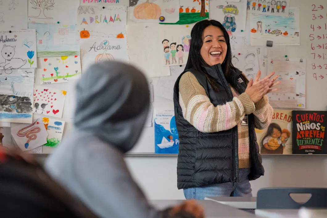 Adriana Alvarez in her classroom in front of a bulletin board. A student in a hoodie is in the foreground.