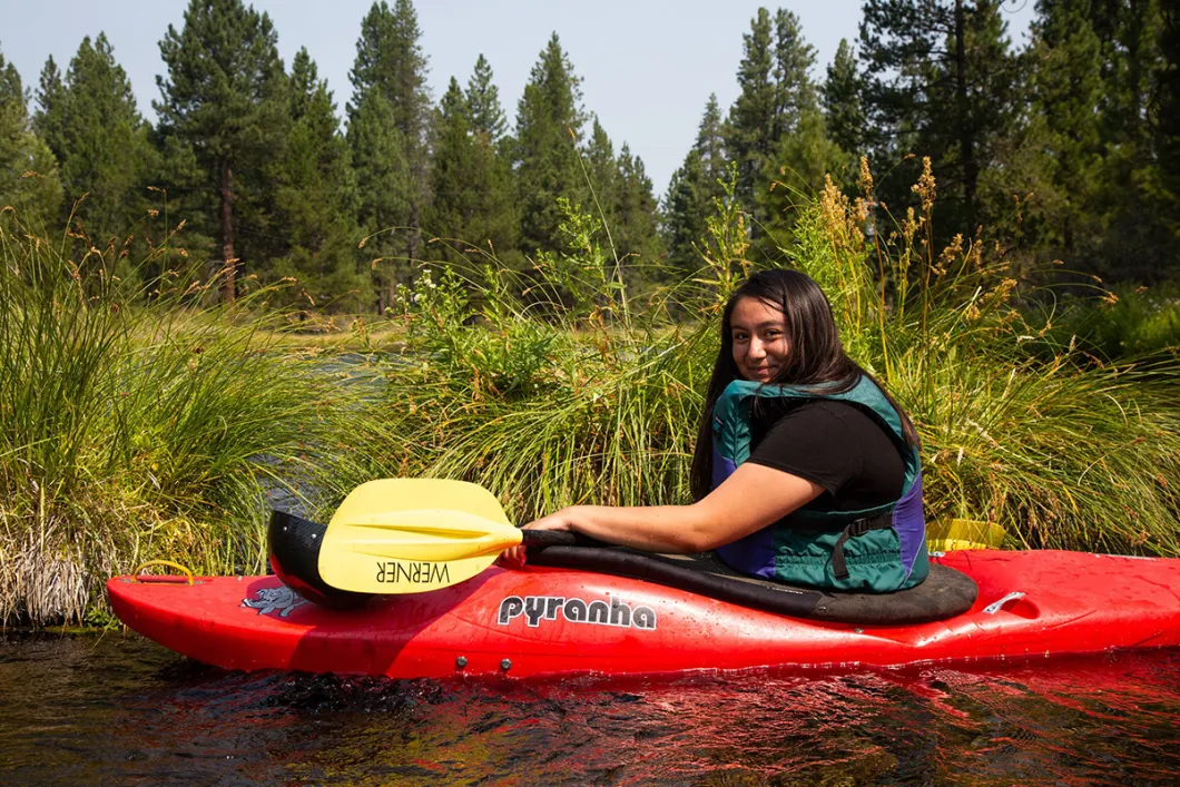 Wilson in a red kayak in the water in front of tall grasses.