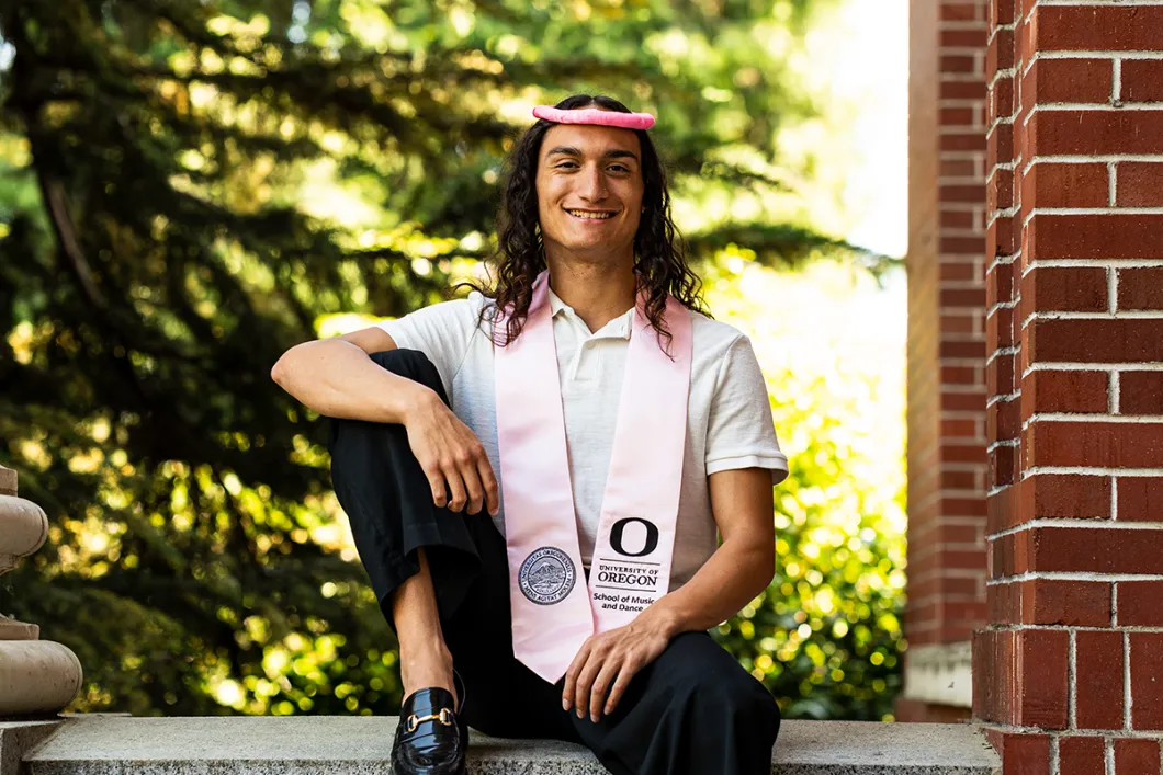 Correa sitting smiling at the camera in a gradutation stole