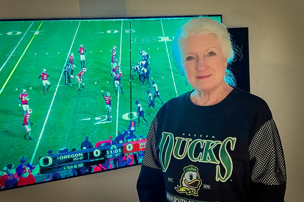 Laurie smiling with the football game behind her with duck gear on