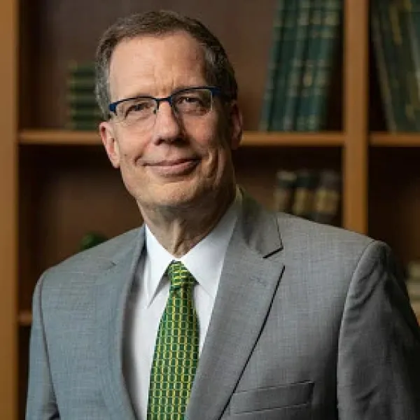 A smiling man with glasses in front of a bookshelf. 