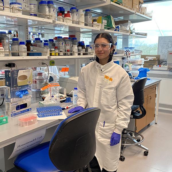 Student in white lab coat and goggles in a lab