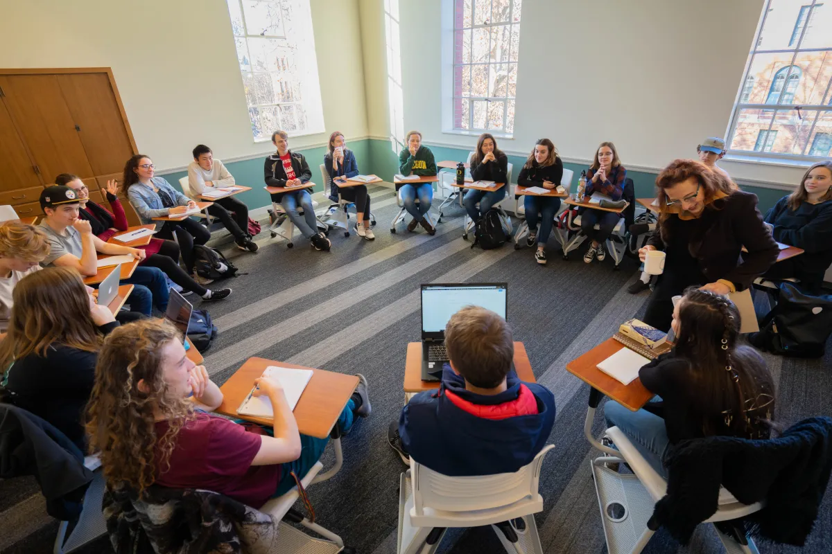 A group of students in a classroom, sitting in desks arranged in a circle