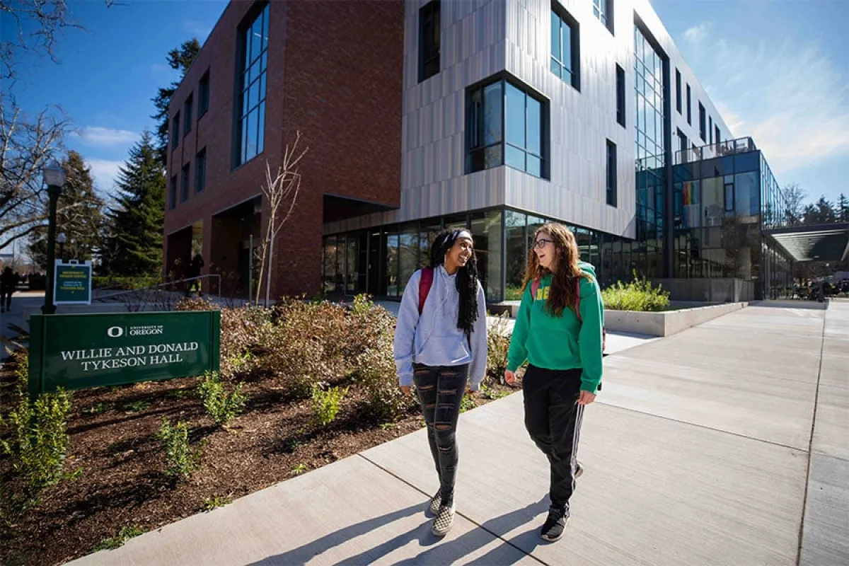 Two students laugh as they walk way from a campus building
