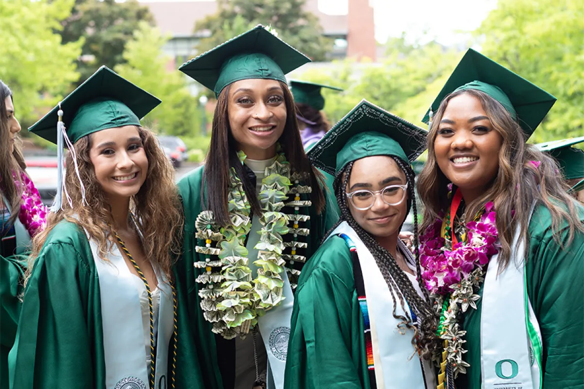 Four UO students in green caps and gowns pose for a photo