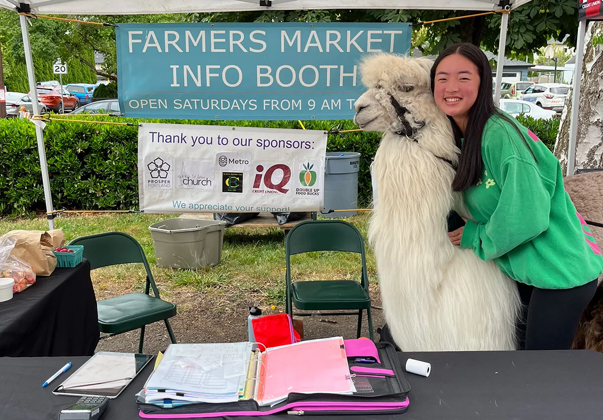 Hailey Yang hugs an alpaca at a farmers market info booth