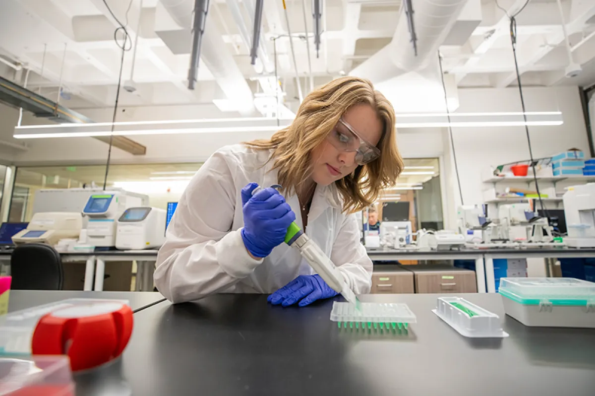 A student works in a lab, using an advanced pipette to put materials into a tray