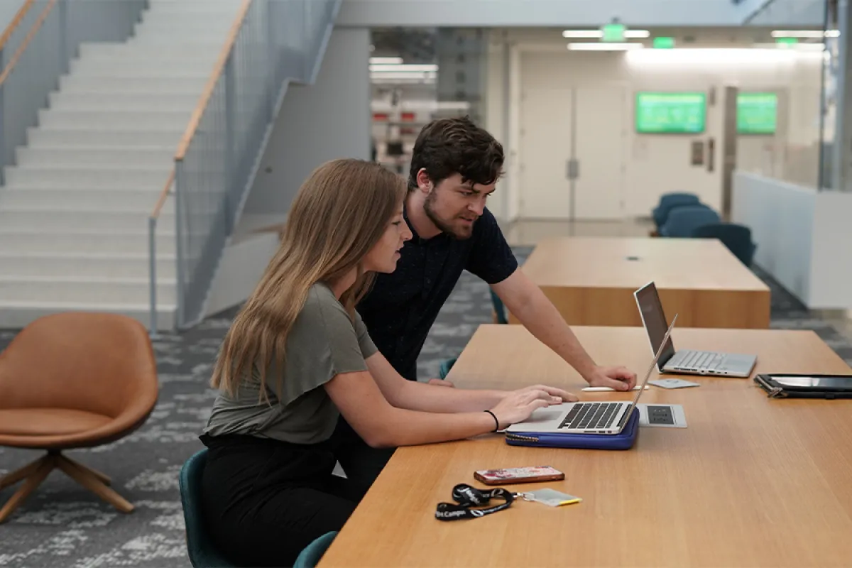 Two UO students look at a laptop together while sitting at a table.
