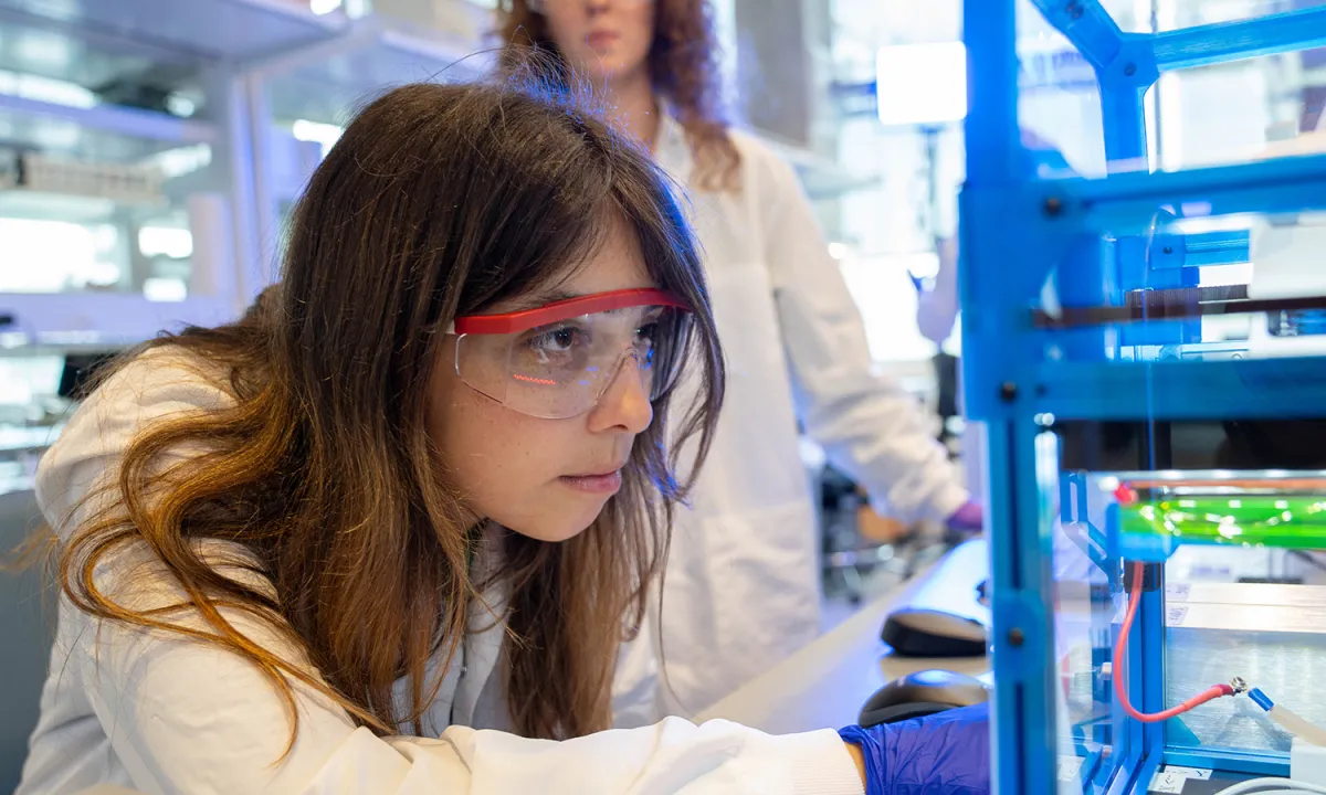 UO student in a lab coat and lab glasses looks at science related materials at Knight Campus