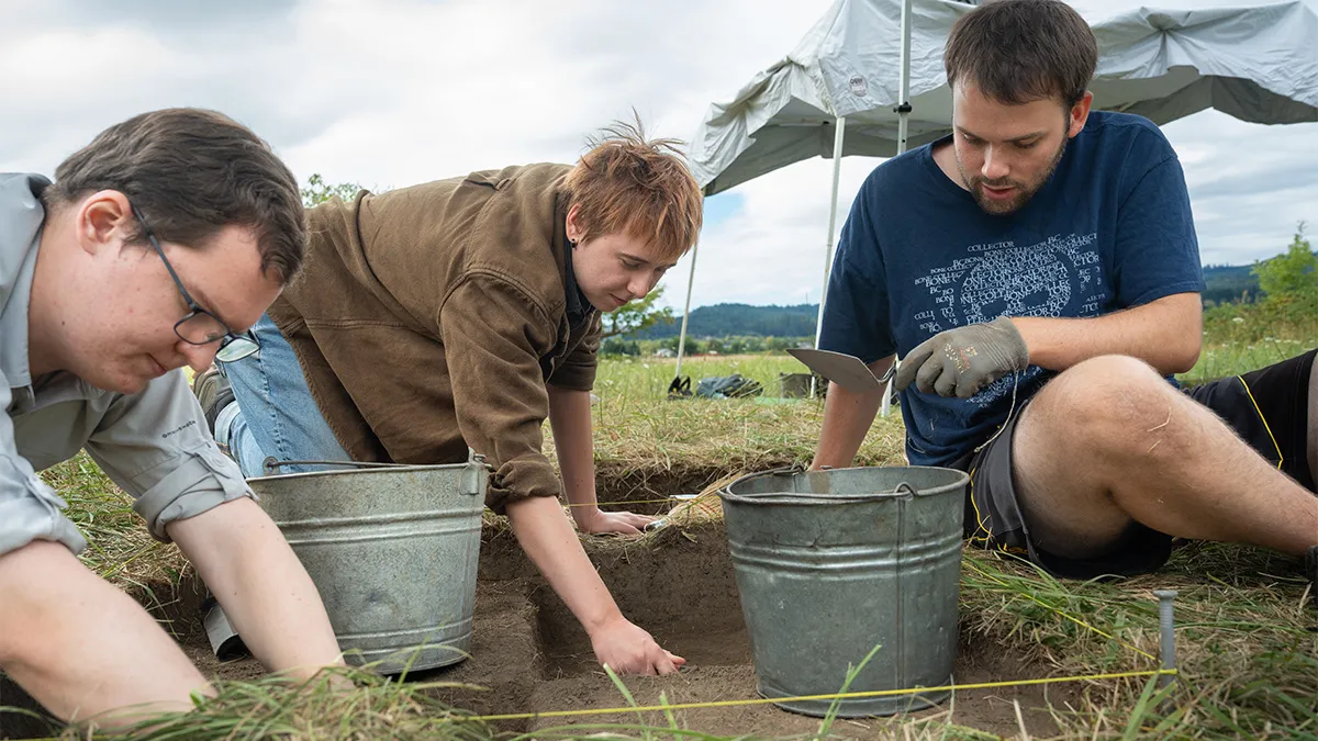 3 students with buckets digging in the dirt outside