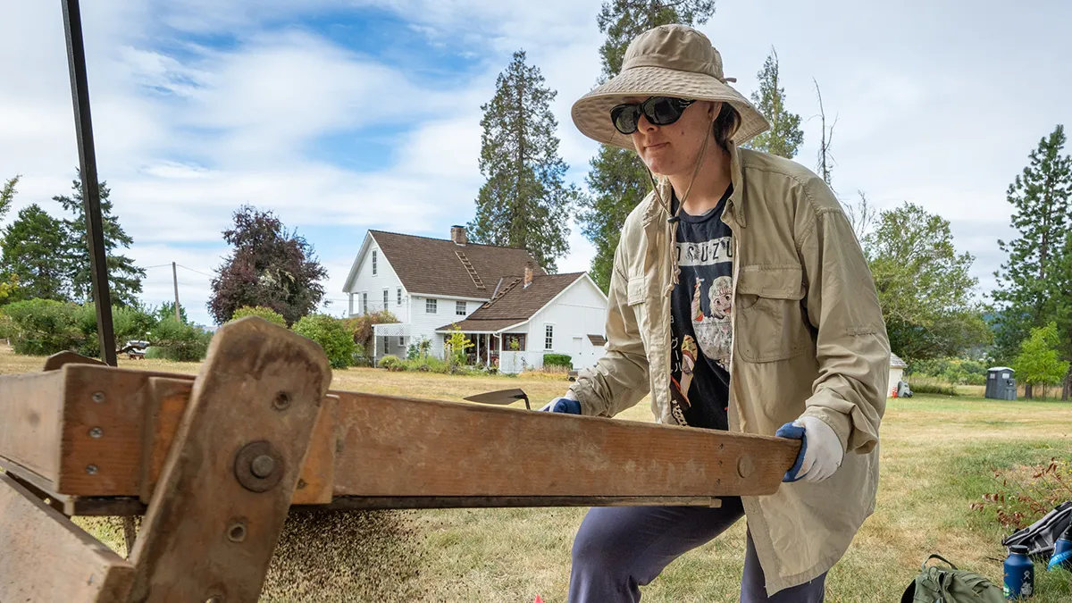 A student in a work hat and jacket working at a wood platform outside