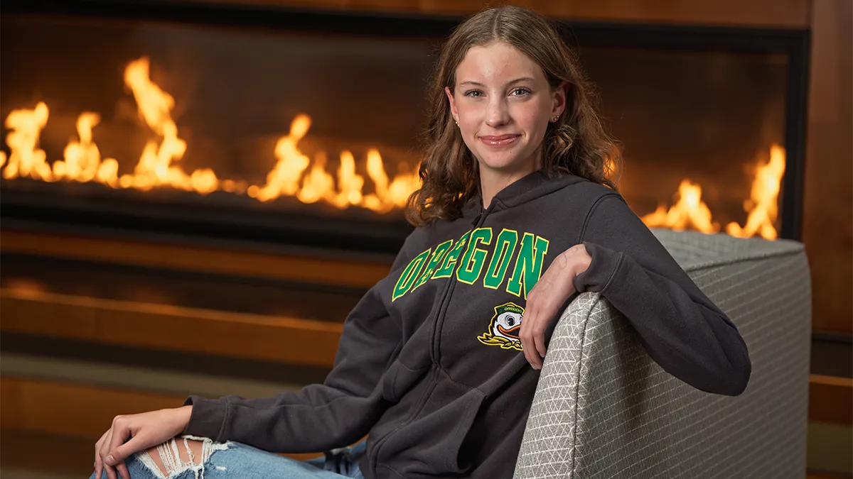 Teen girl in Oregon apparel sitting in front of a hearth