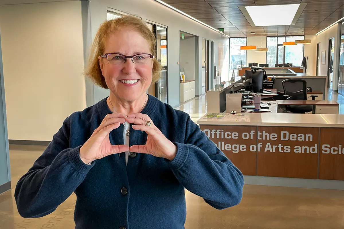 Natalie Poole throwing an O standing the the College of Arts and Sciences Office of the Dean