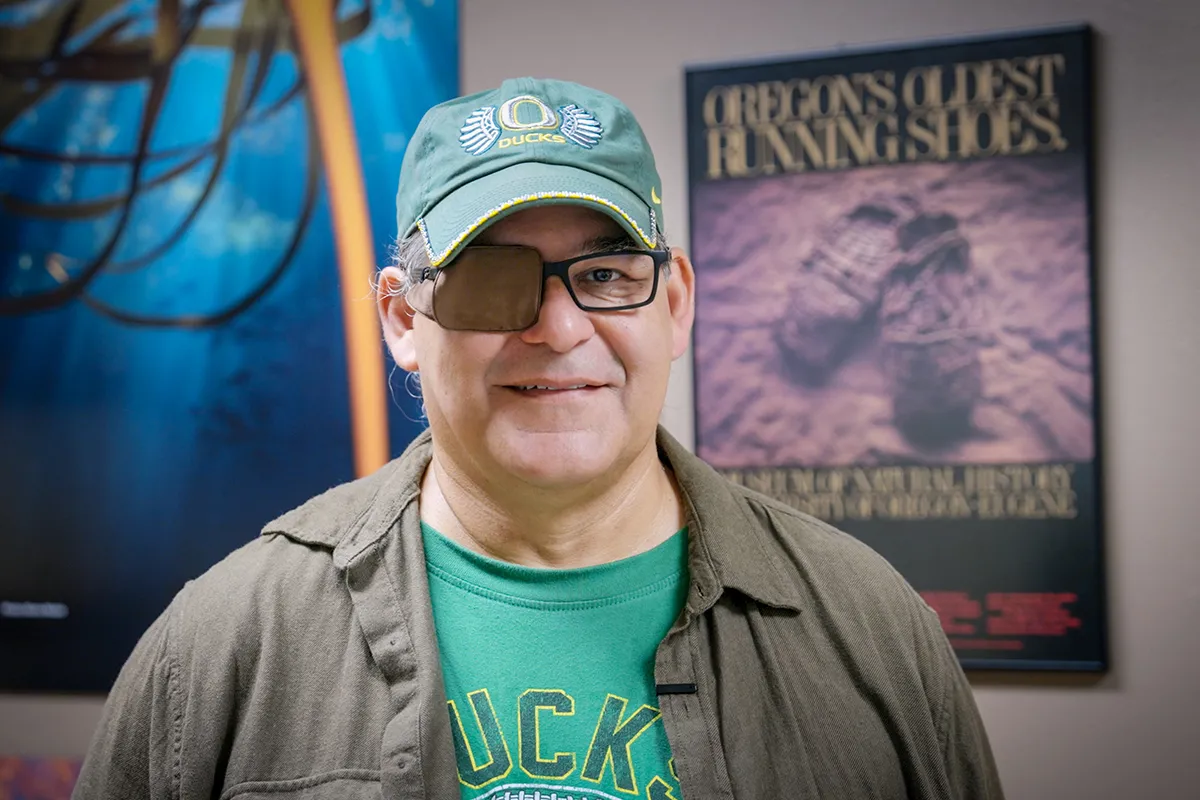 David Lewis stands in front of a poster of the world's oldest shoes at the UO Museum of Natural and Cultural History