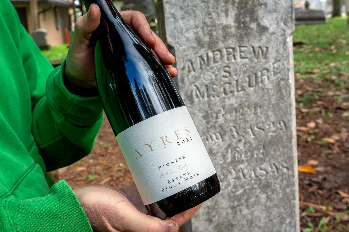 Holding bottle of Ayres wine with Andrew McClure grave stone in background