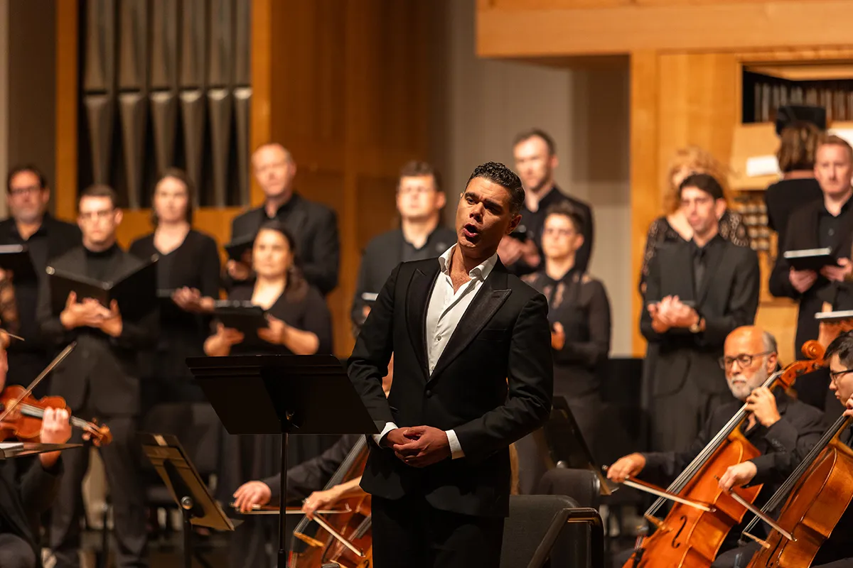 A man singing in front of musicians and a choir on the Beall Hall stage