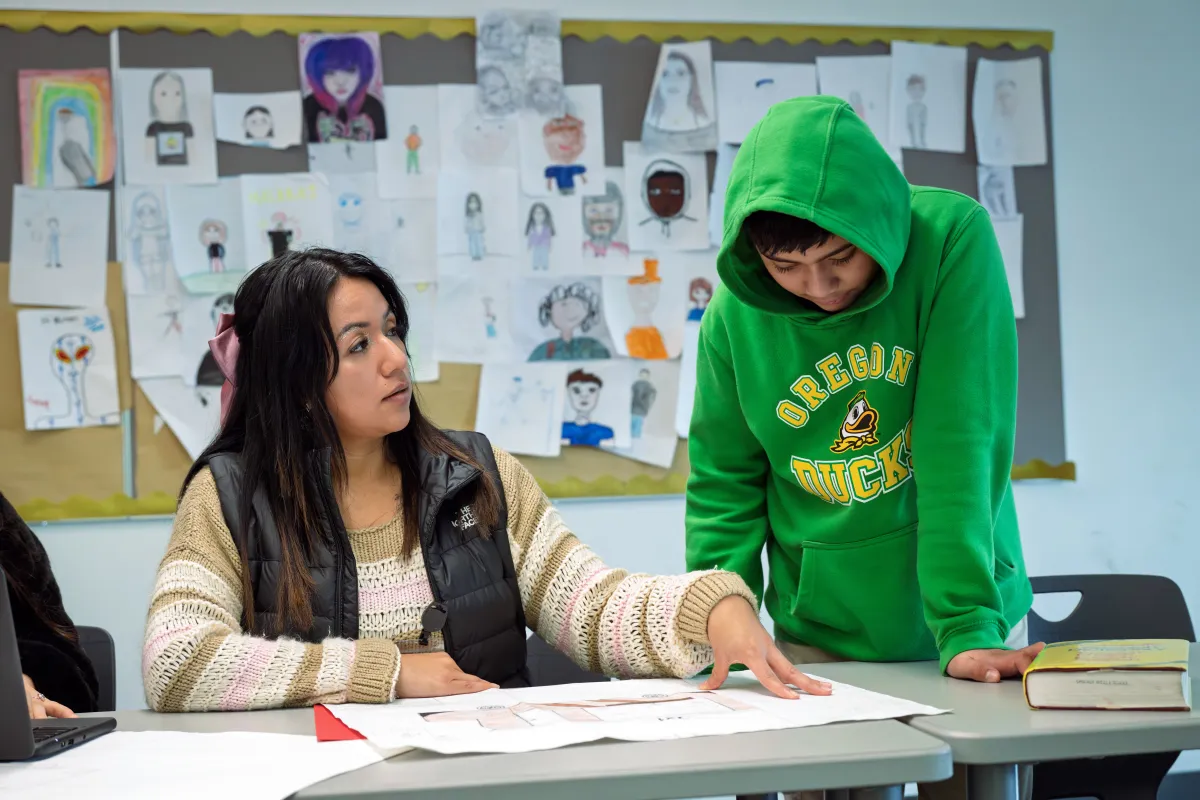 A woman with long dark hair speaks to a student wearing a hoodie